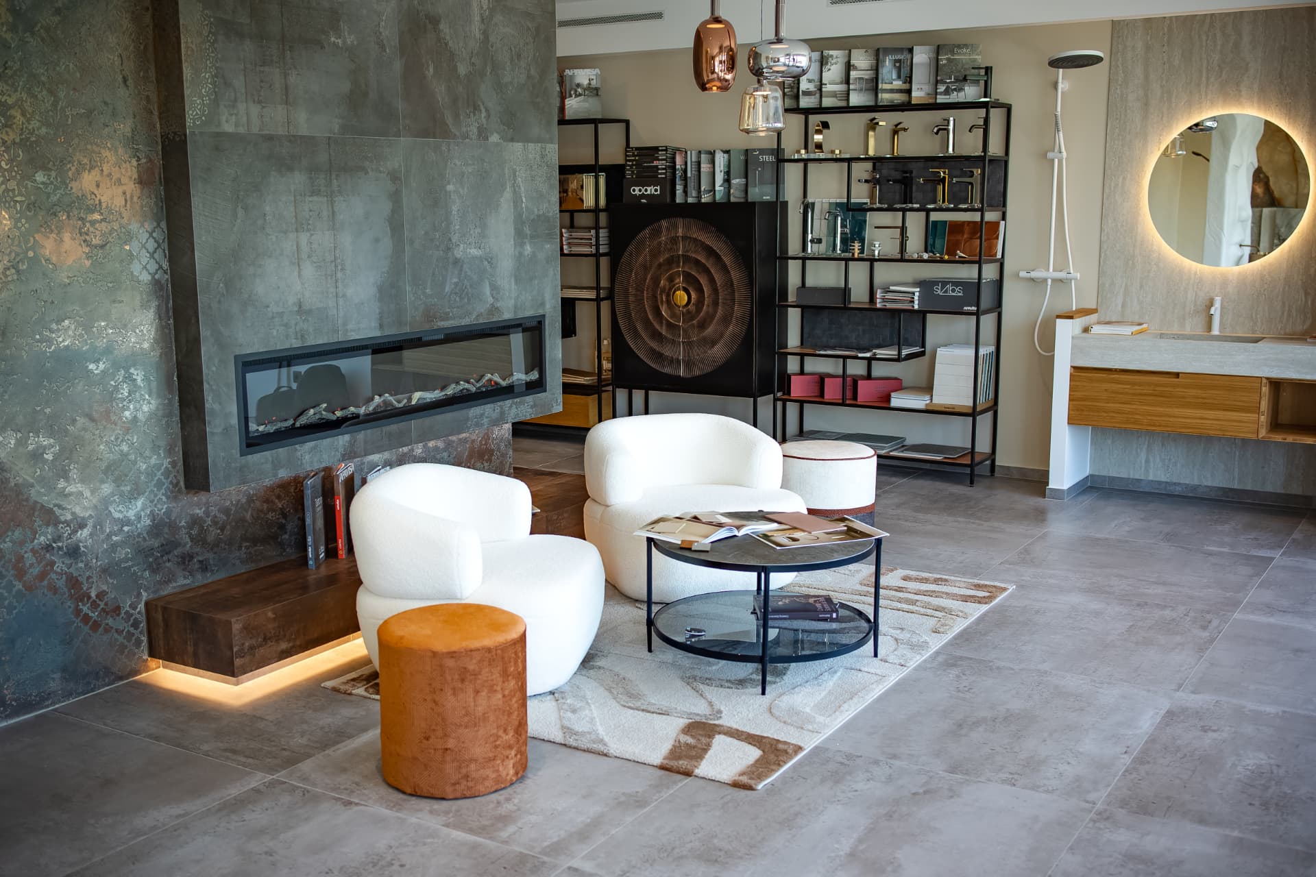 Loungebereich im Schauraum mit Kaminwand, zwei hellen Sesseln und Materialregalen im Hintergrund